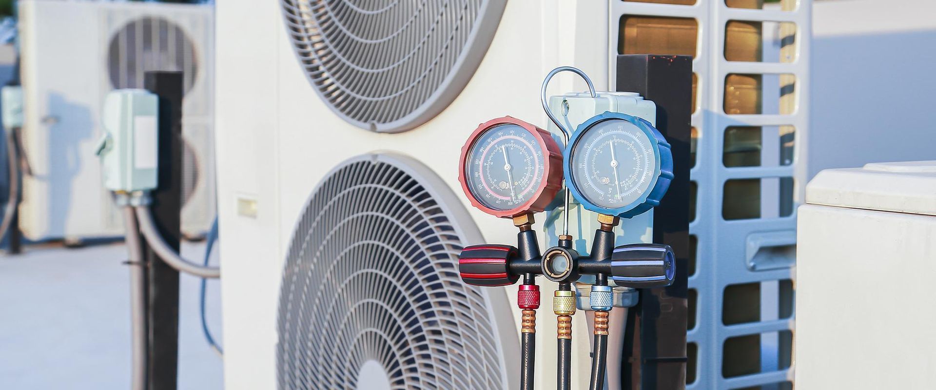 Blue and red gauges on HVAC service manifold connected to an outdoor air conditioning unit