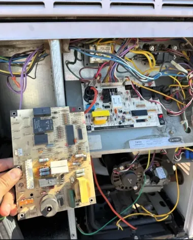 Hand holding a circuit board inside an open appliance with exposed wires and components