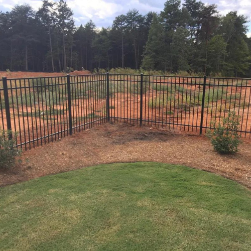 a metal fence surrounds a lush green lawn in a backyard .