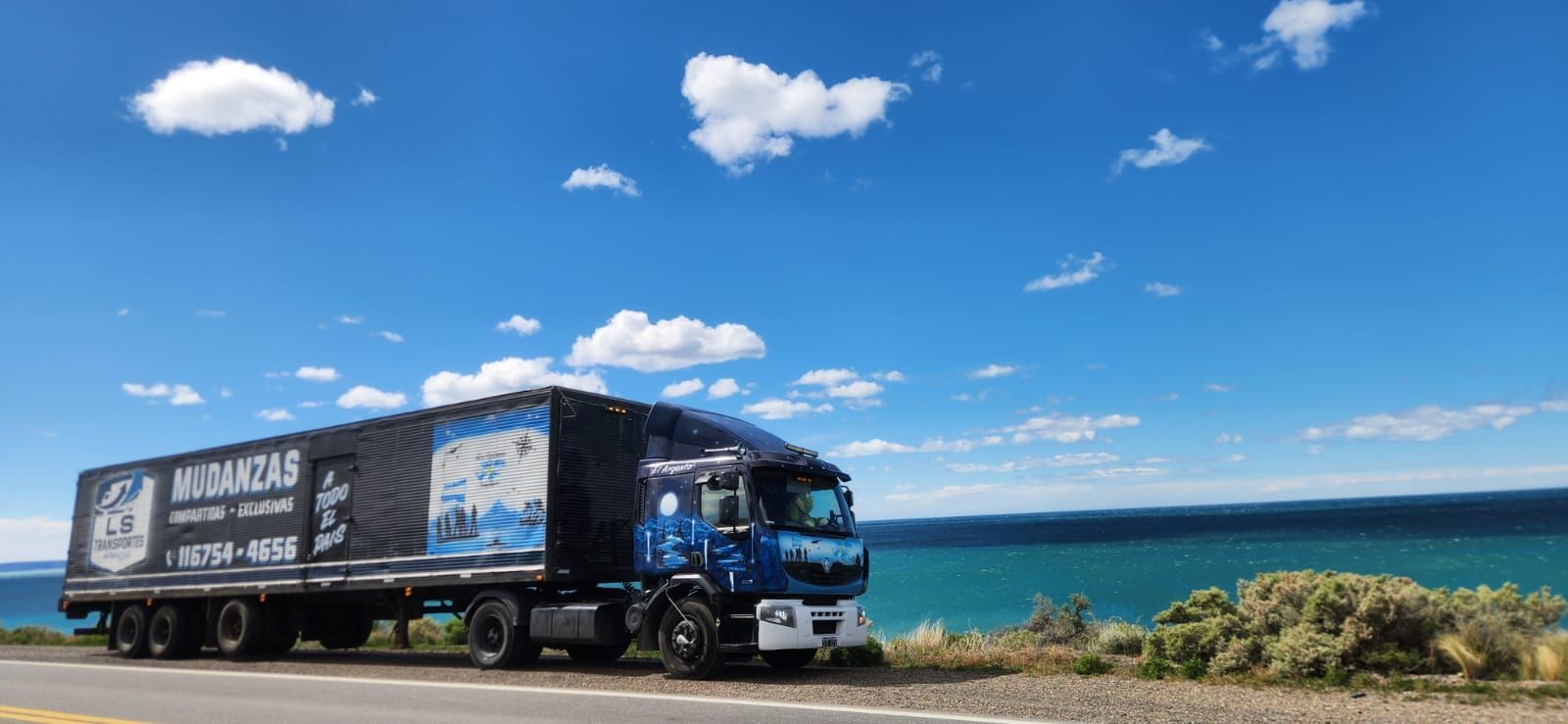 Camión estacionado cerca del océano, bajo un cielo azul con nubes.