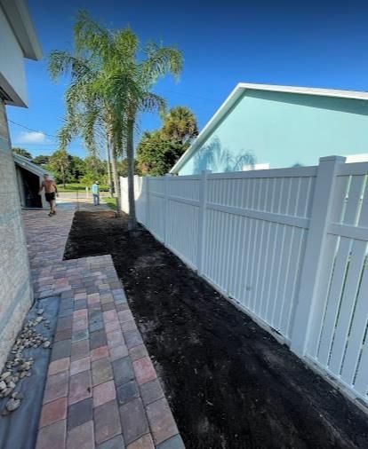A white fence surrounds a brick walkway next to a house.