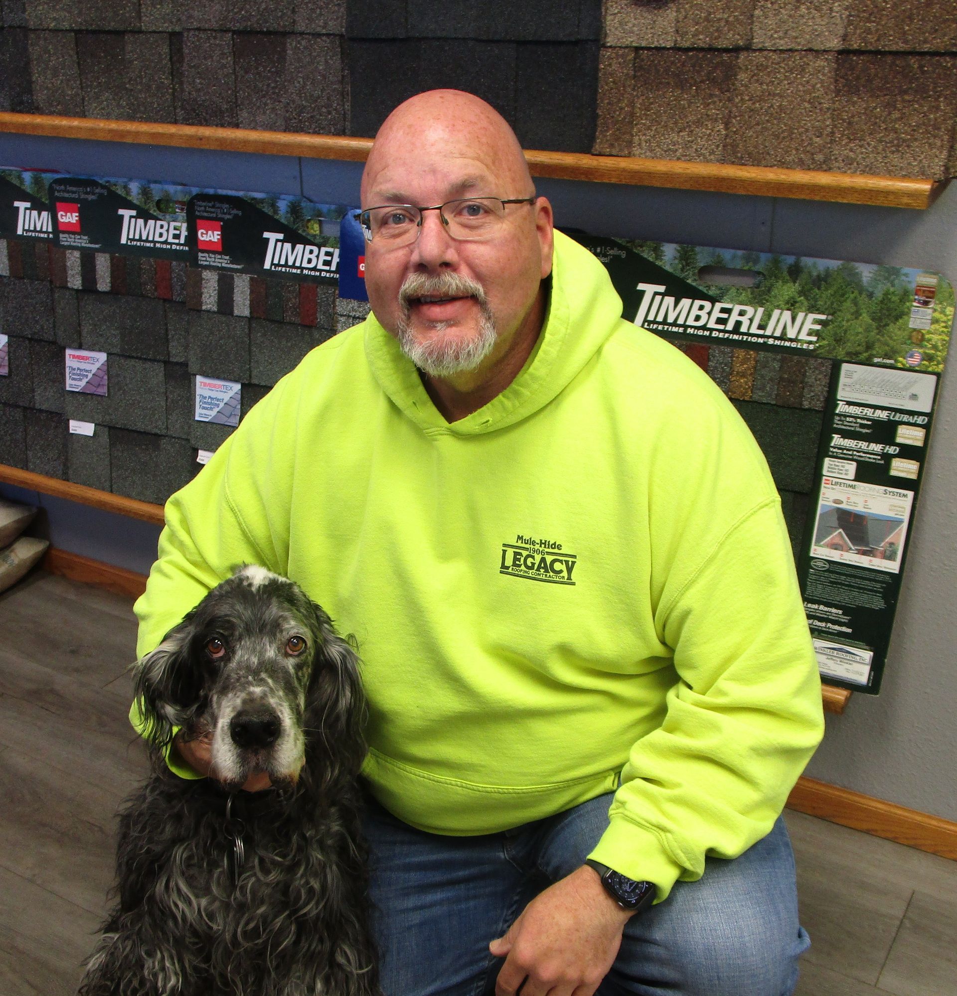 A man in a yellow hoodie is kneeling down next to a dog