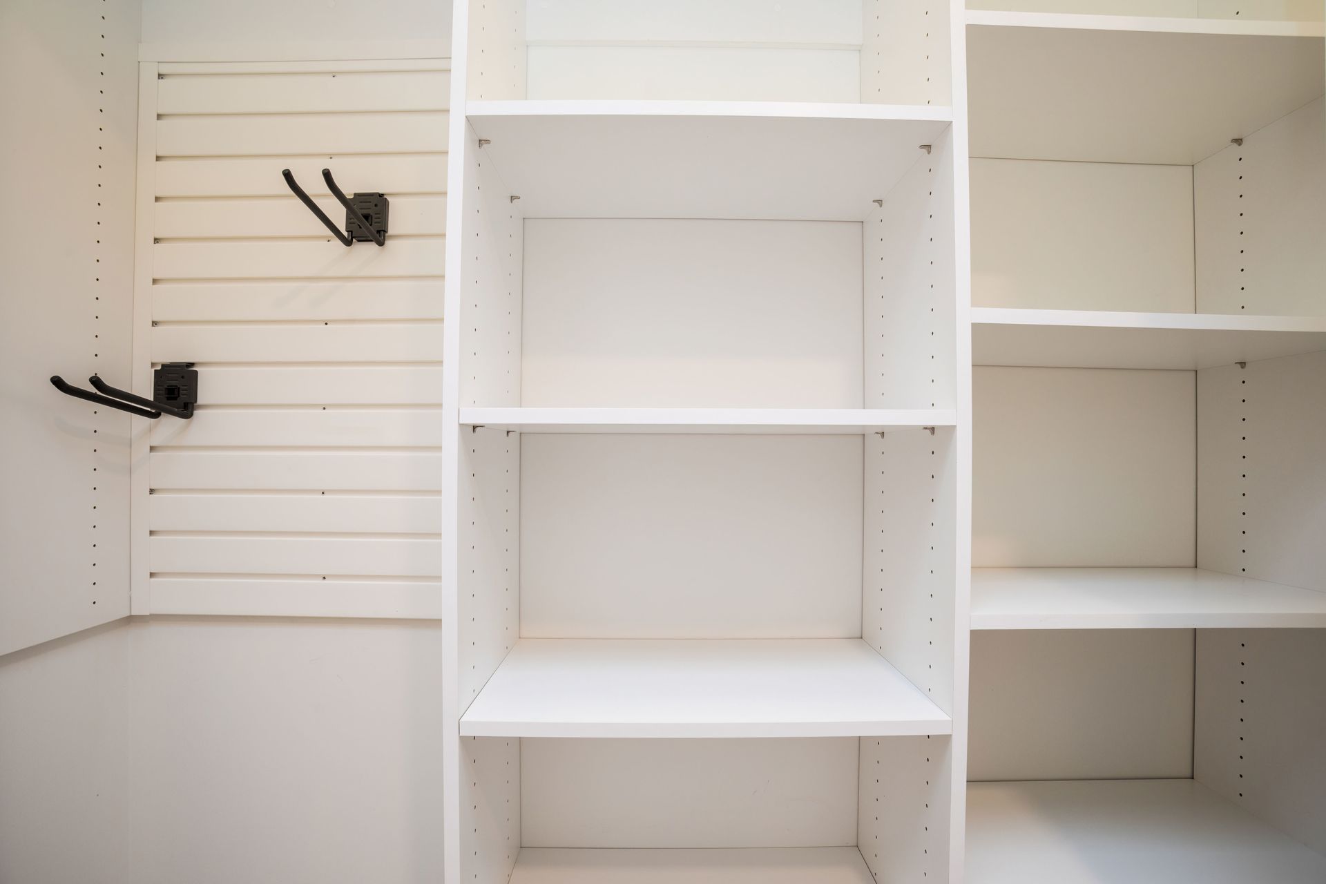 A closet with empty shelves and hooks on the wall.