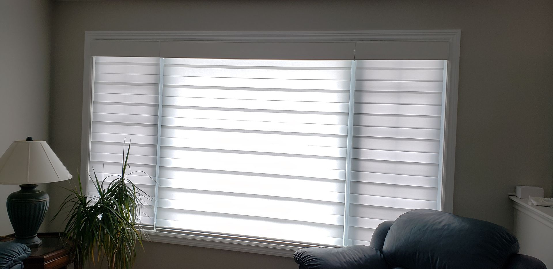 A living room with a large window and white blinds.