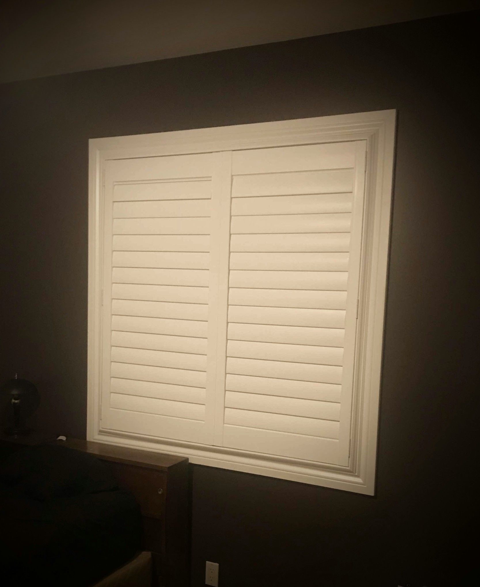A window with white shutters on it in a dark room.