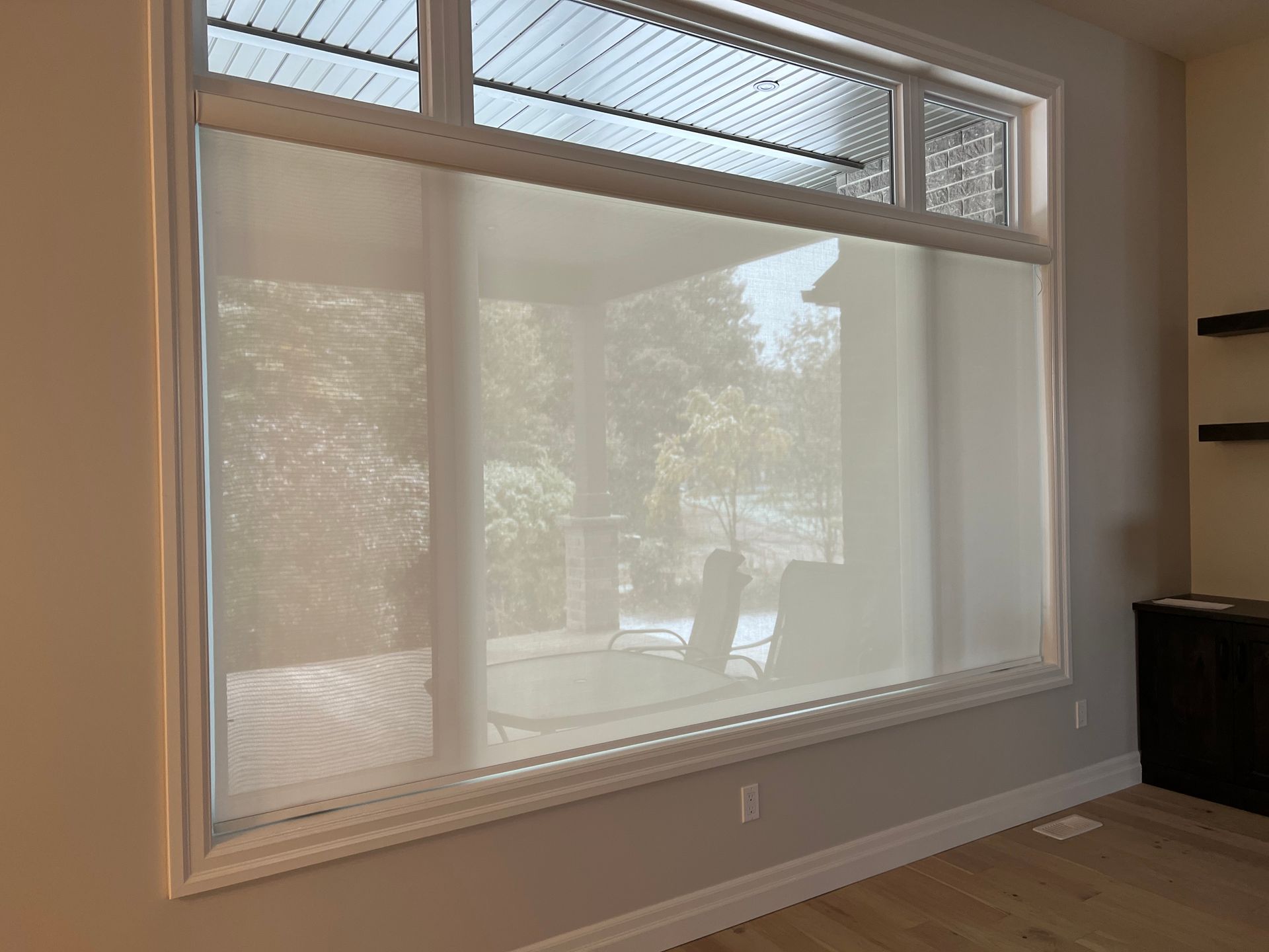 A large window with a white blind on it in a living room.