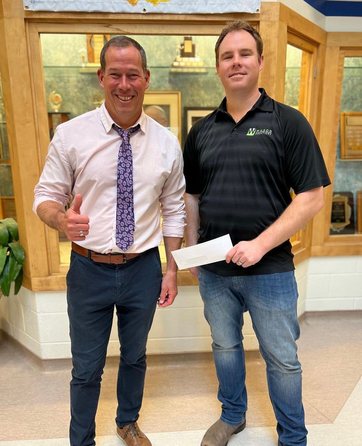 Two men are standing next to each other and one is holding a check