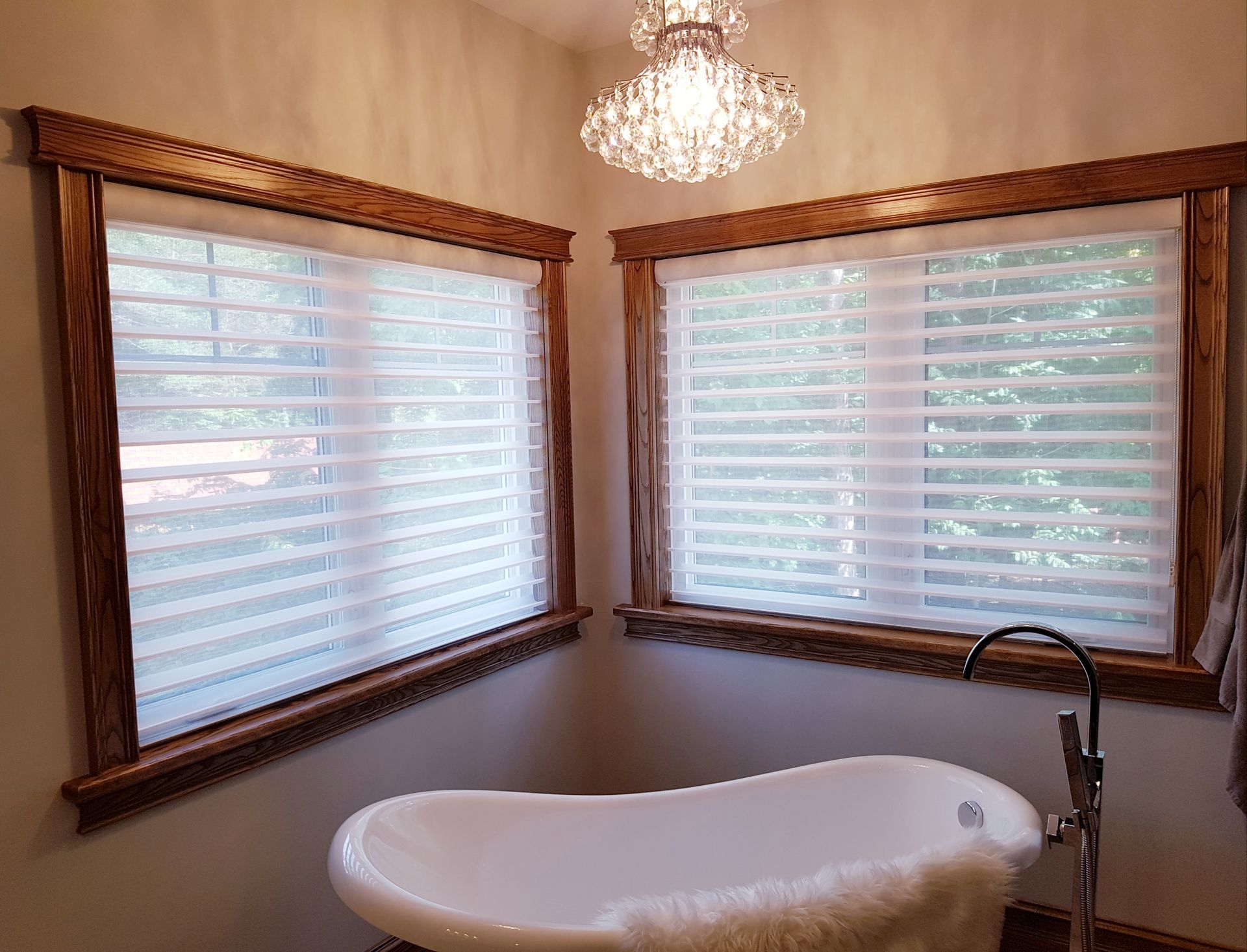 A bathroom with a bathtub , two windows and a chandelier.
