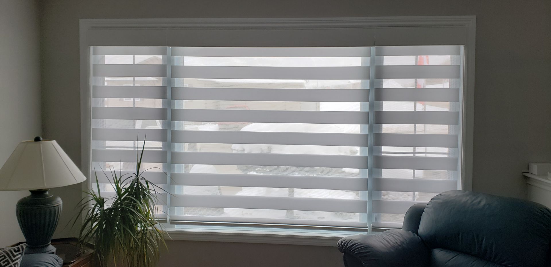 A living room with a large window with blinds and a lamp.