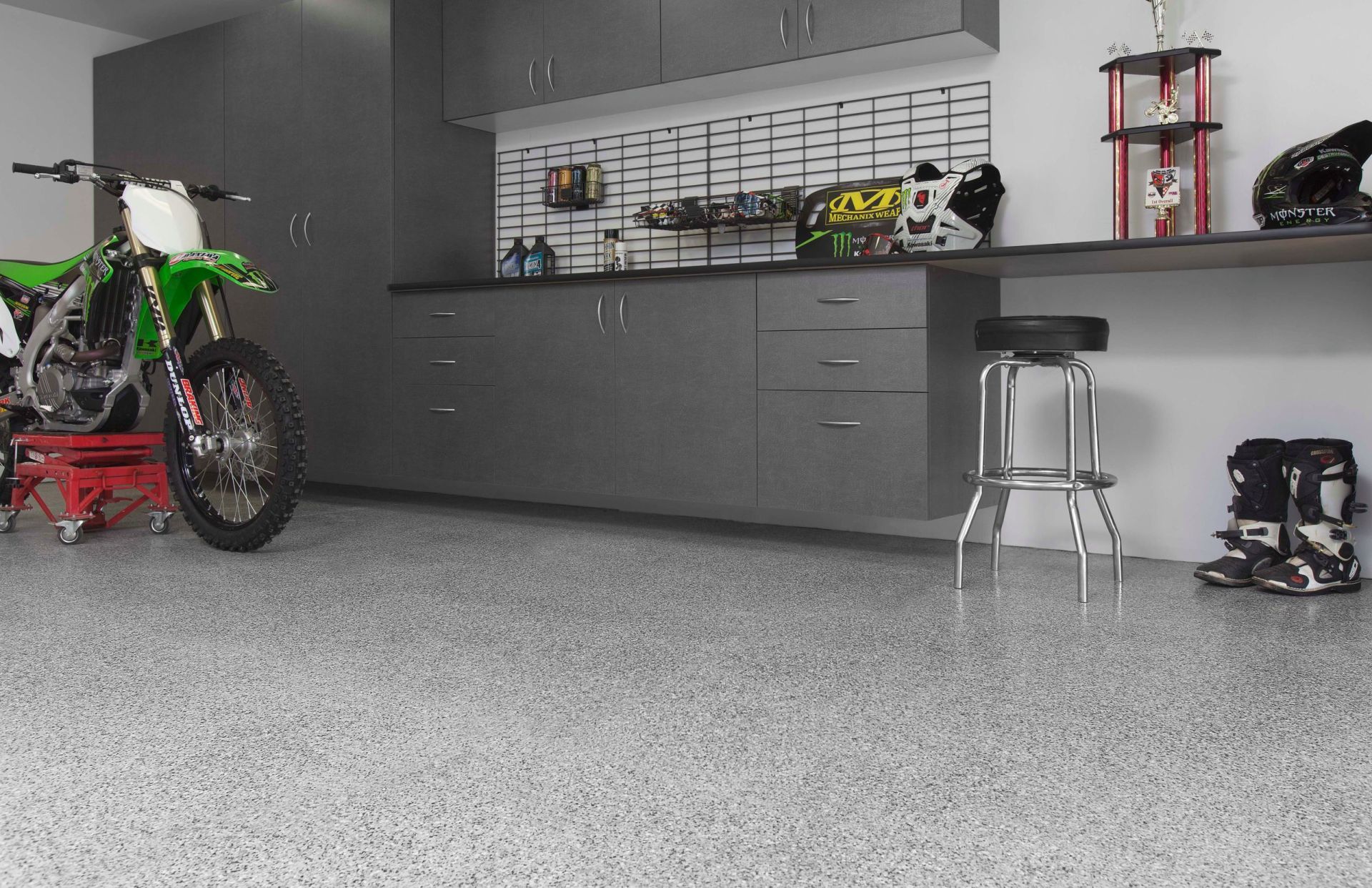 A green dirt bike is parked in a garage next to a stool.
