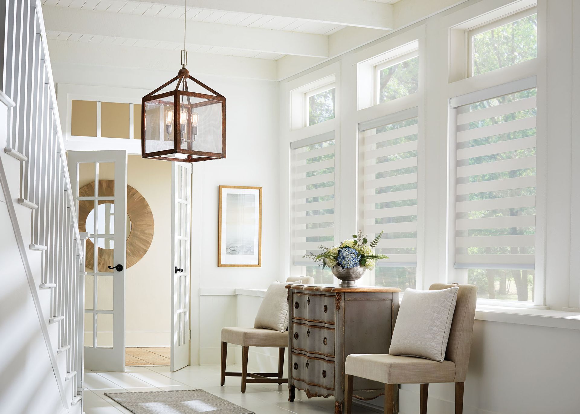 A hallway with stairs , chairs , a dresser and a lantern hanging from the ceiling.