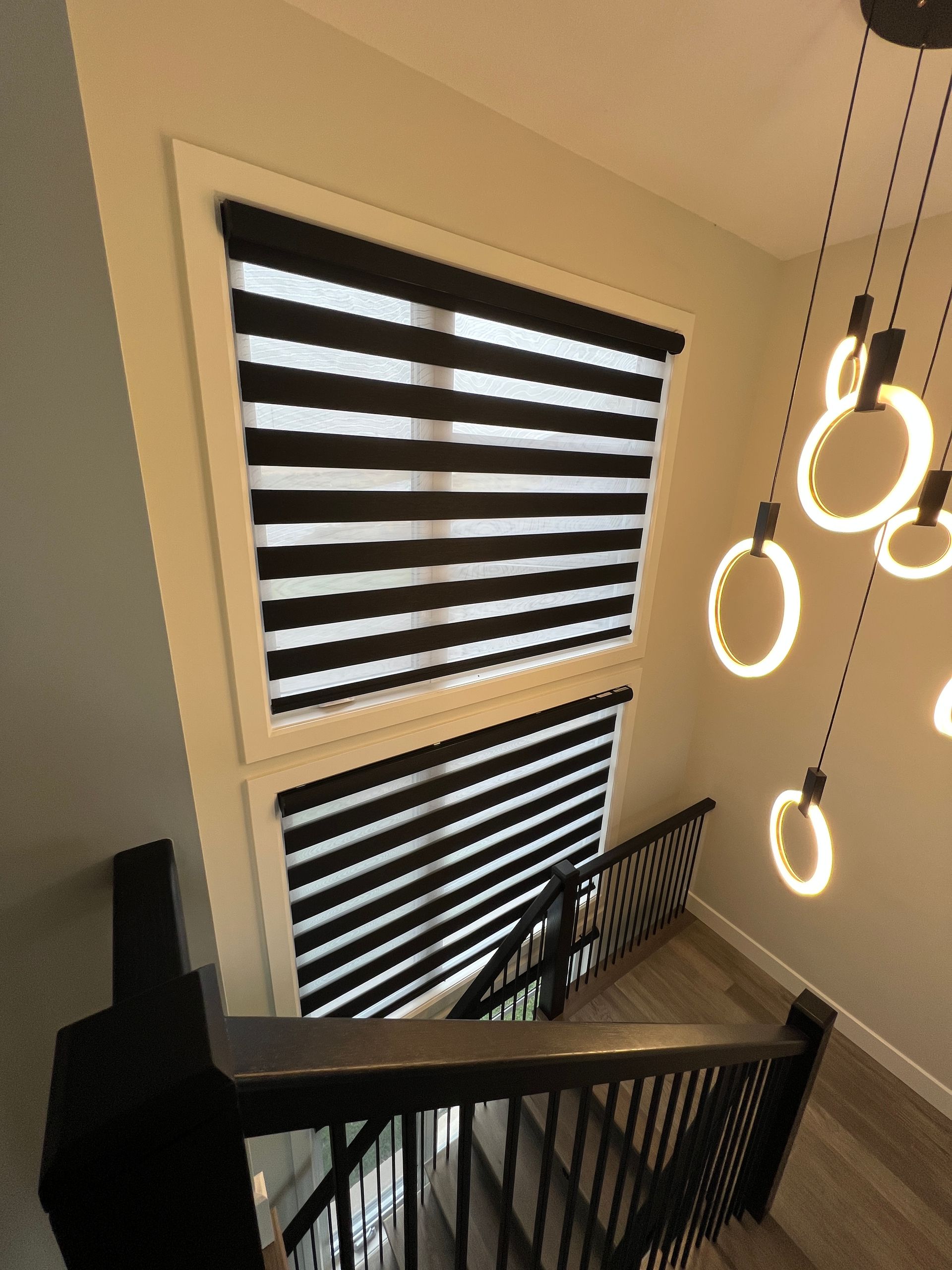 A staircase with black and white striped blinds and a chandelier hanging from the ceiling.