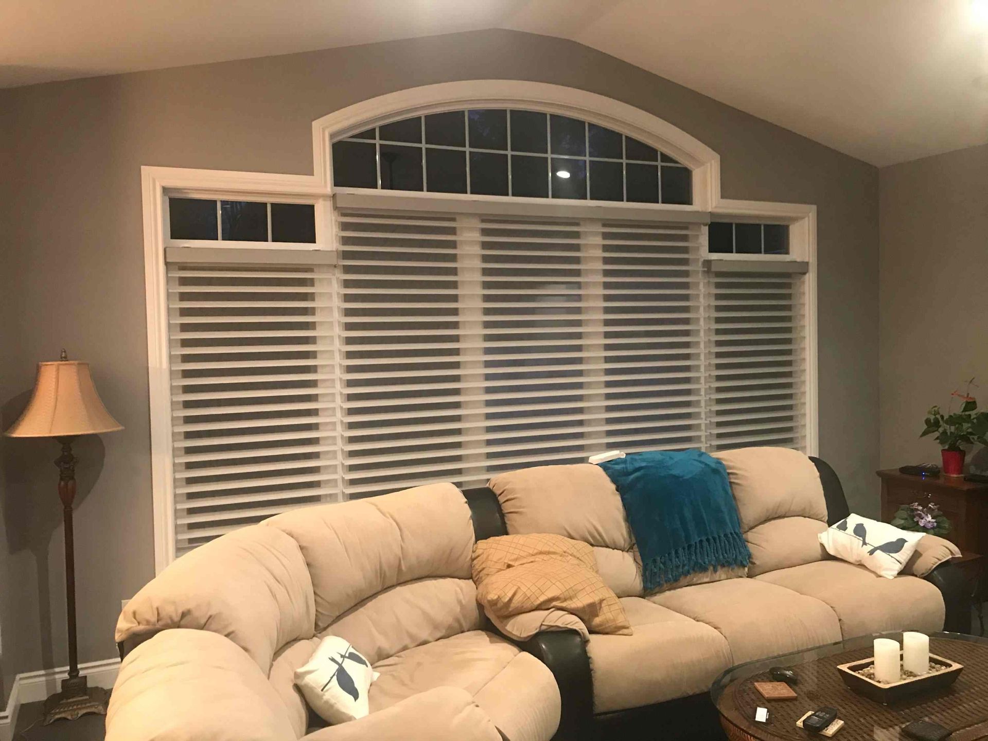A living room with a large couch and shutters on the windows.