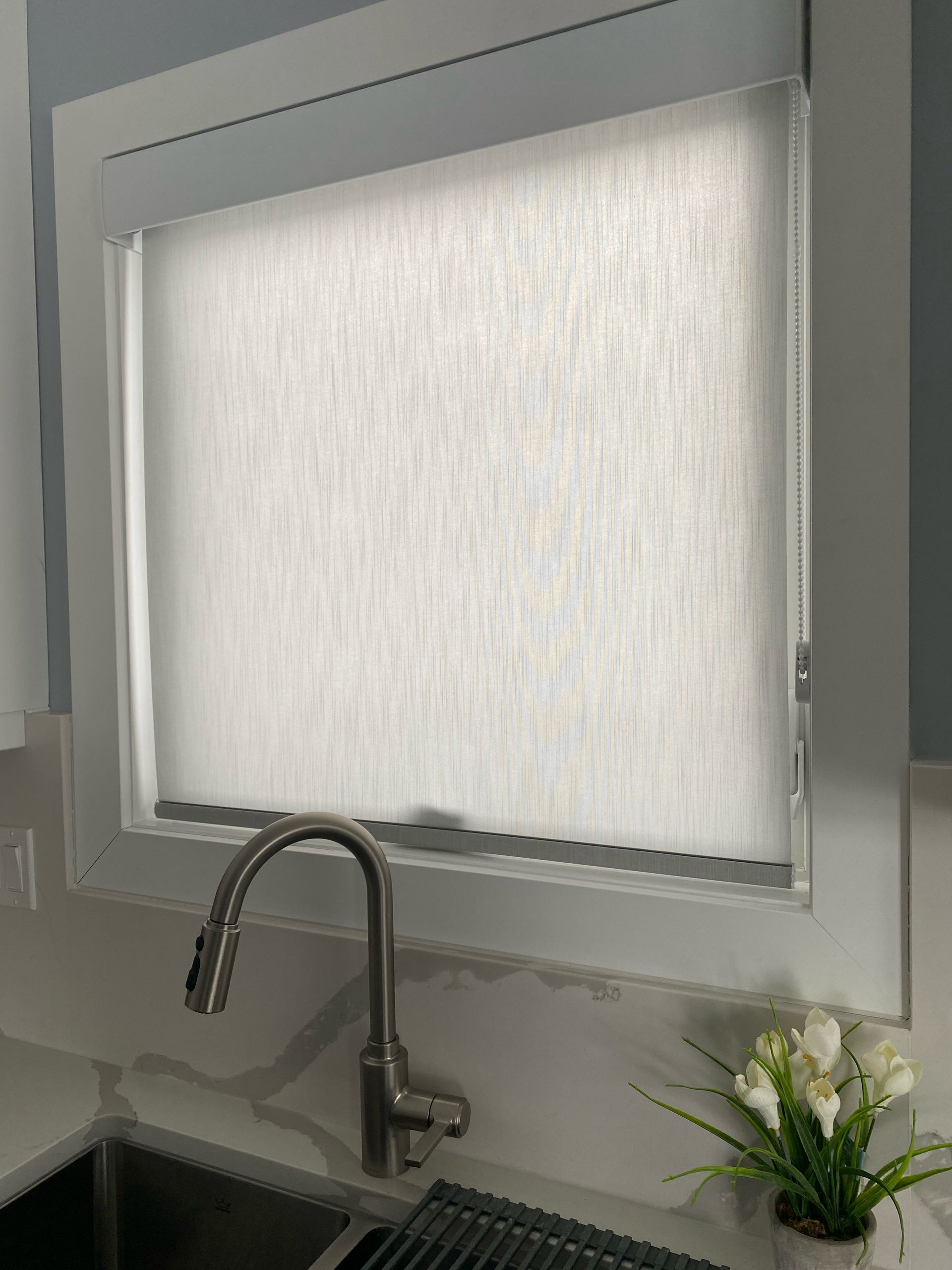 A kitchen window with a white blind and a sink.