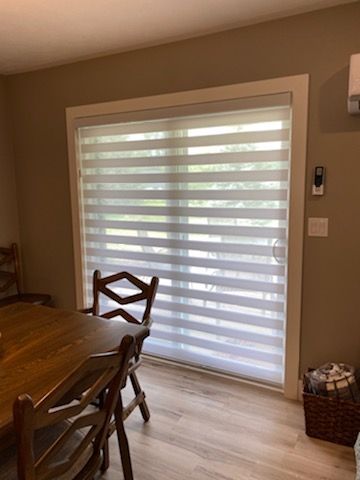 A dining room with a table and chairs and a sliding glass door with blinds.