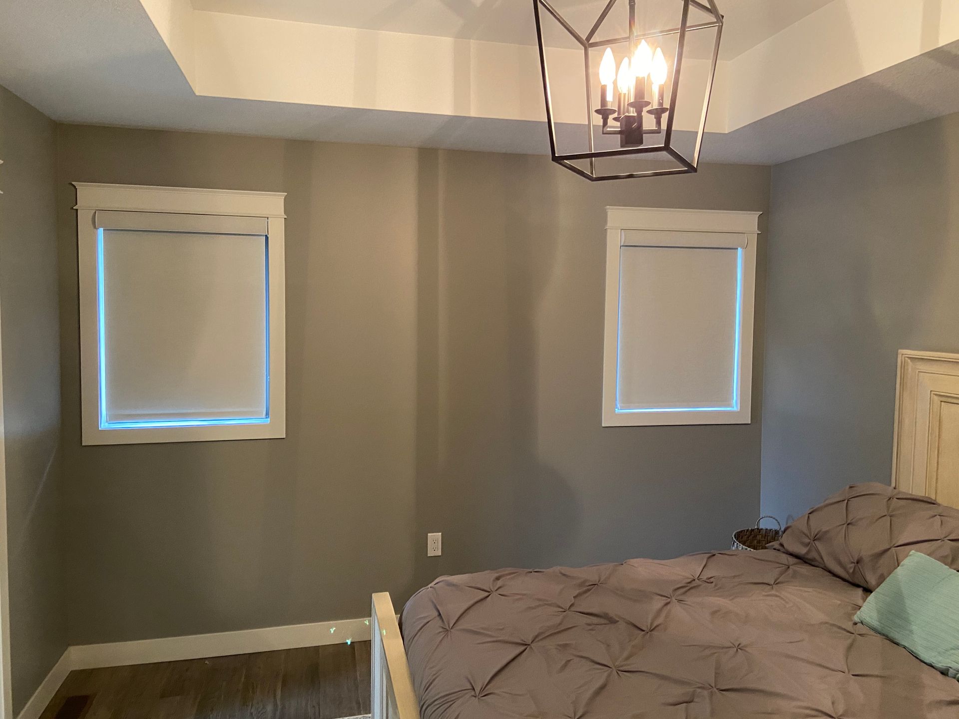 A bedroom with a bed , two windows and a chandelier.