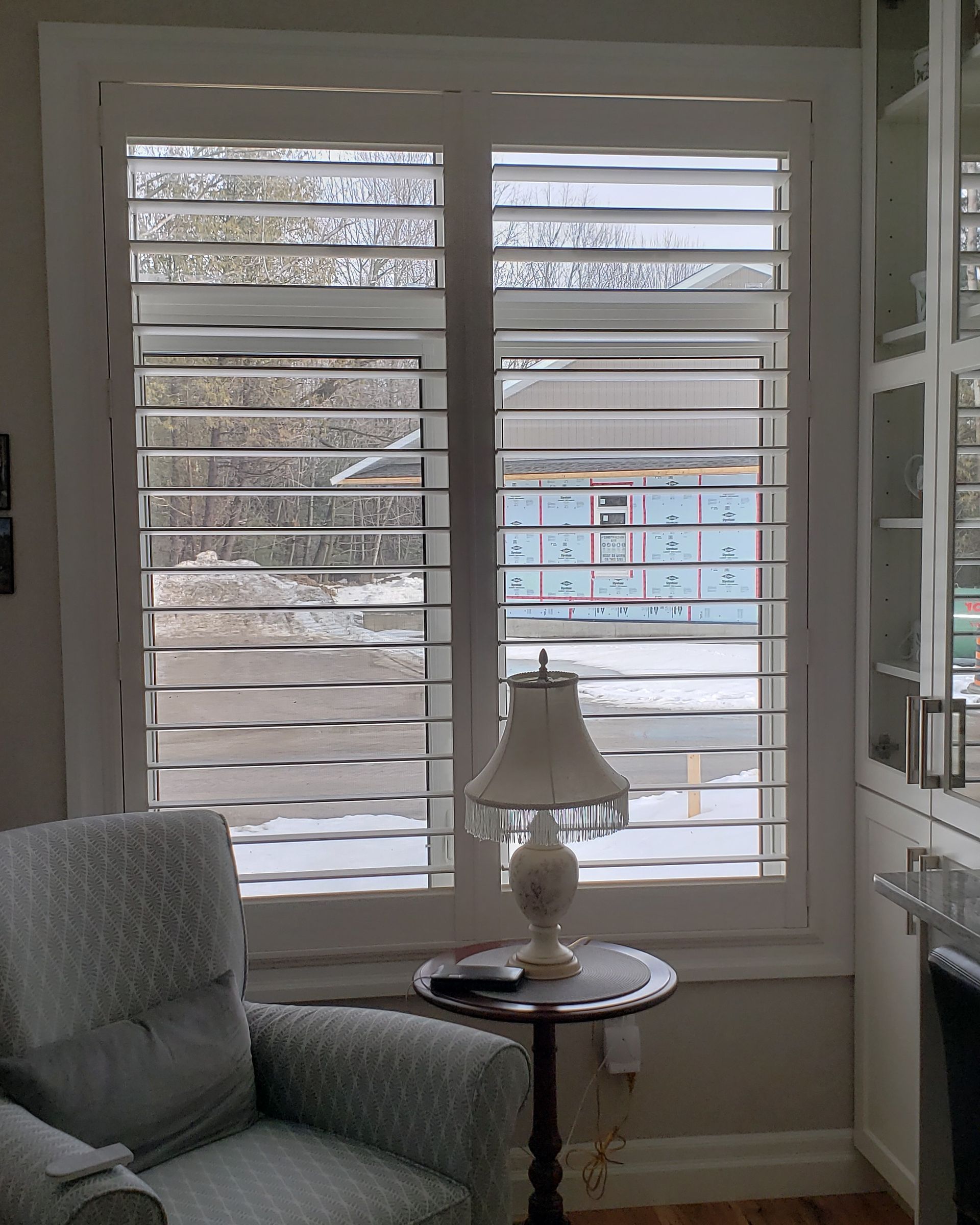 A living room with a chair and a lamp in front of a window with shutters.