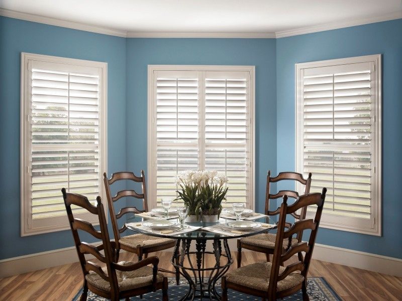 A dining room with a table and chairs and shutters on the windows.