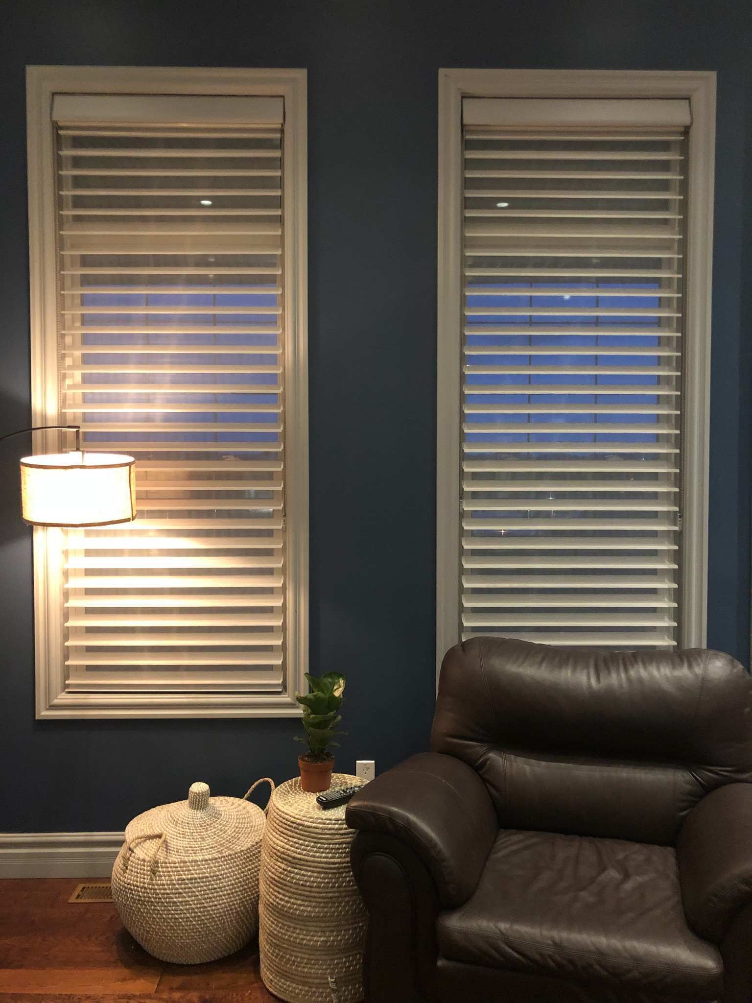 A living room with two windows , a chair and a lamp.