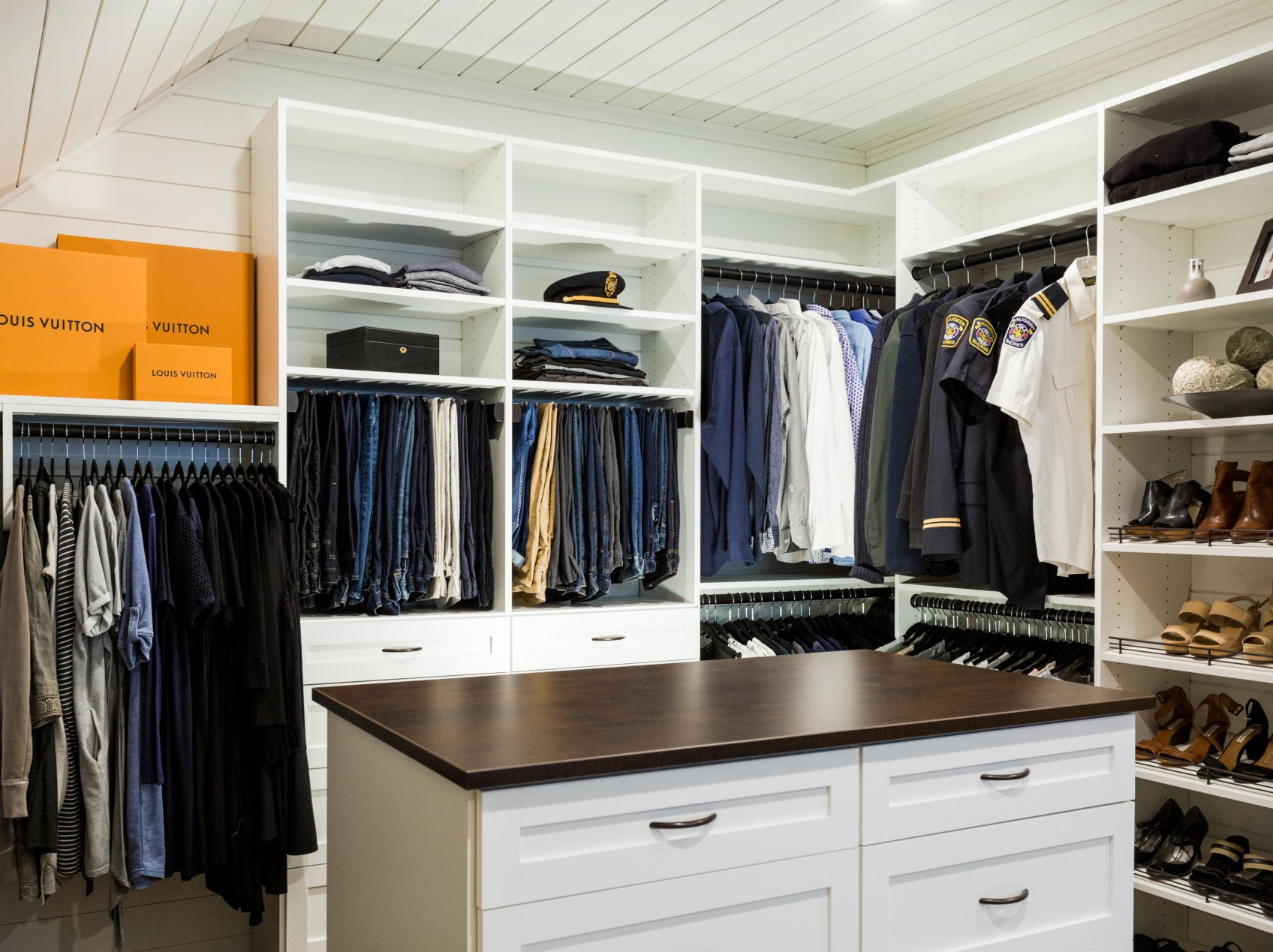 A walk in closet with lots of clothes and a large island in the middle.