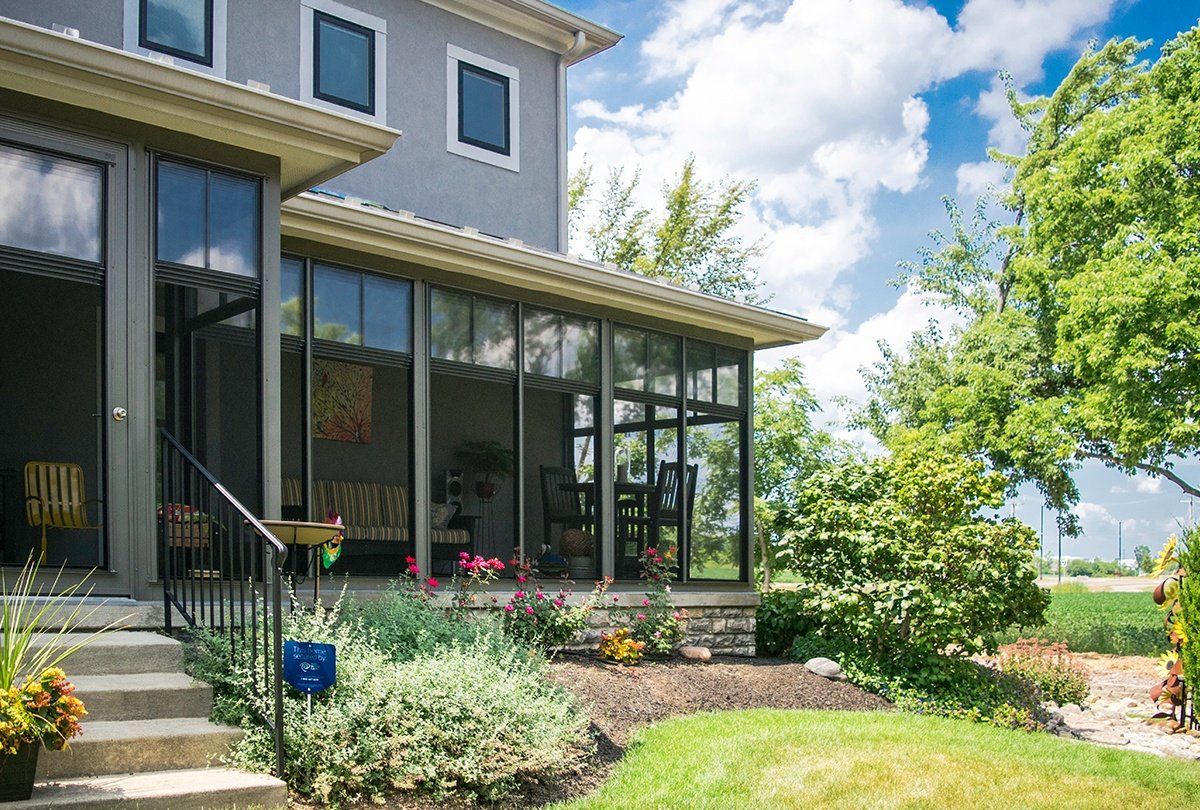 A house with a screened in porch and a large lawn in front of it.