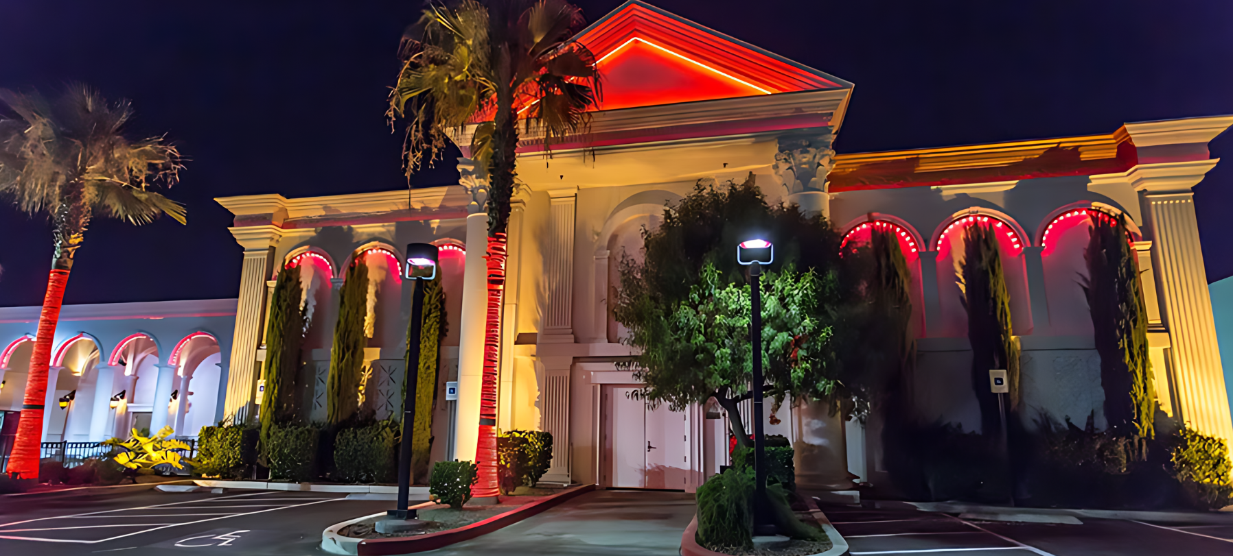 A large building with palm trees in front of it is lit up at night.