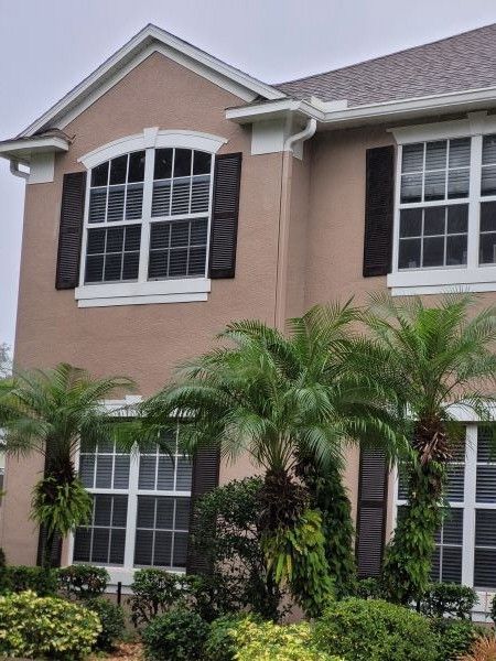 Two-story beige house with white-trimmed windows and palm trees in front