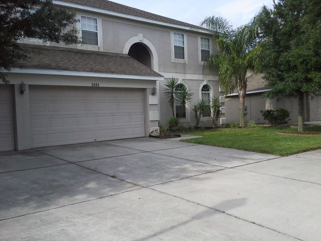Tan two-story house with white trim and dark shutters.