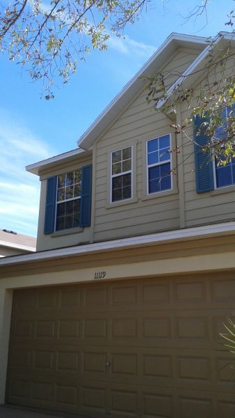 Tan two-story house with tan garage door, blue shutters on windows.