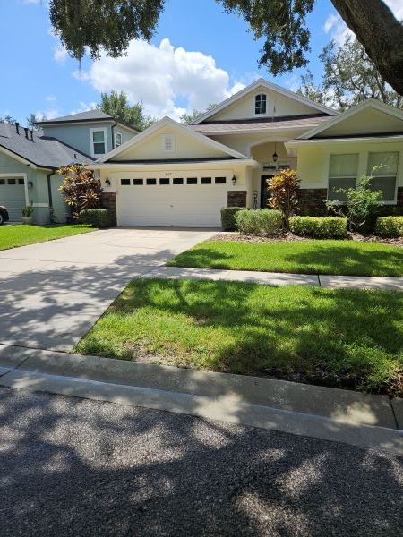 A light yellow house with a white garage door, green lawn, and a driveway. 