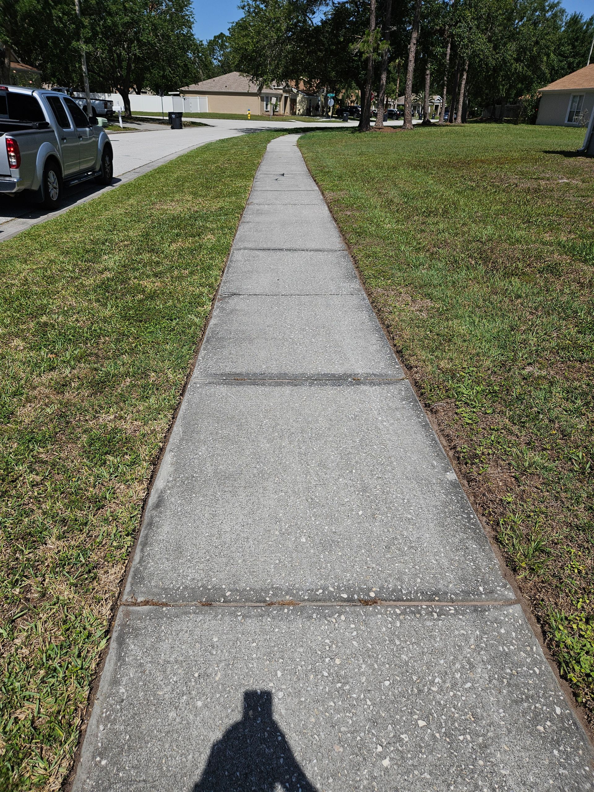 A shadow of a person is cast on a sidewalk next to a grassy field.