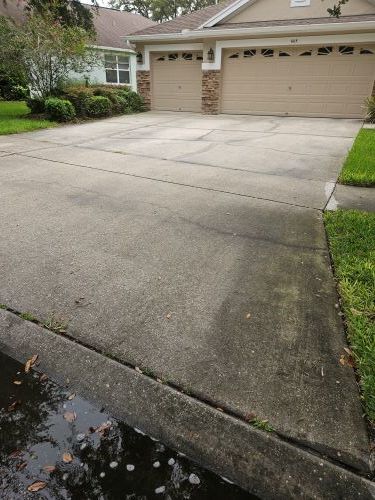 Concrete driveway leading to a house with beige garage doors. Wet concrete borders the curb.
