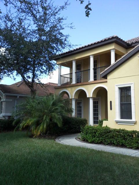 Yellow stucco house with white columns and a second-story balcony.