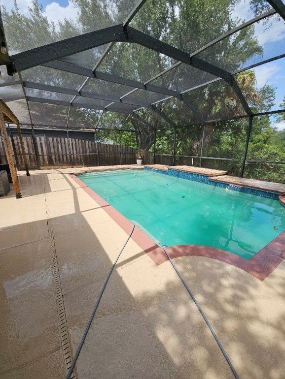 Screened backyard pool with turquoise water, tan deck, and trees beyond the enclosure