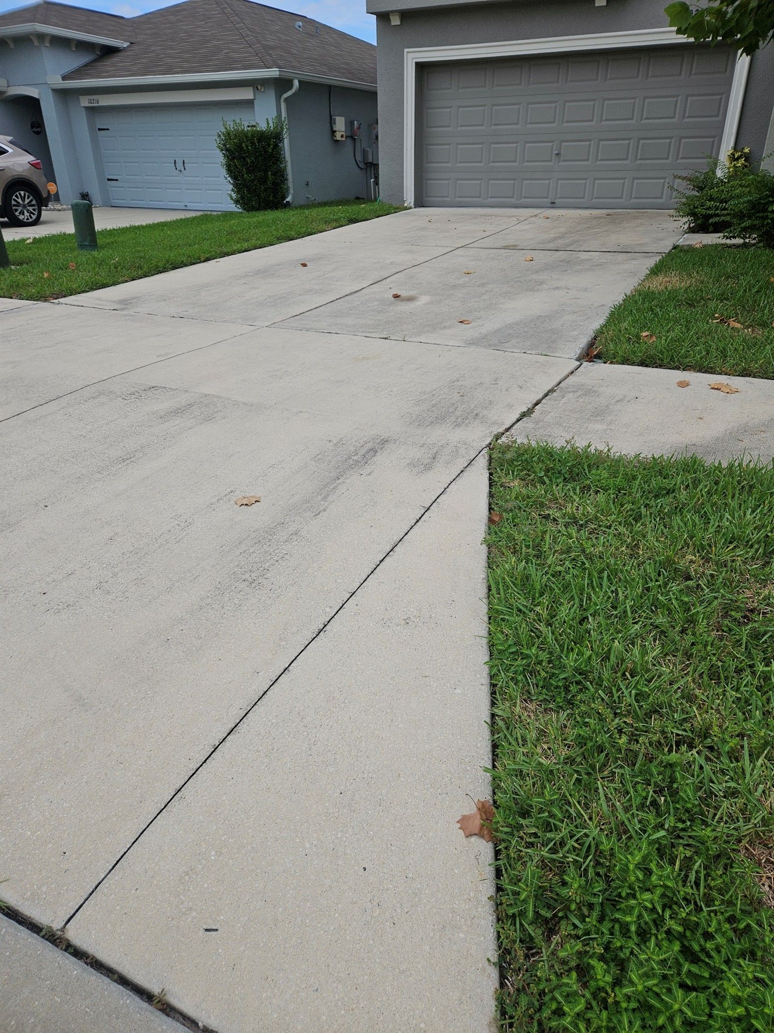 A wide, gray concrete driveway leading to a closed residential garage door, flanked by patches of green lawn.