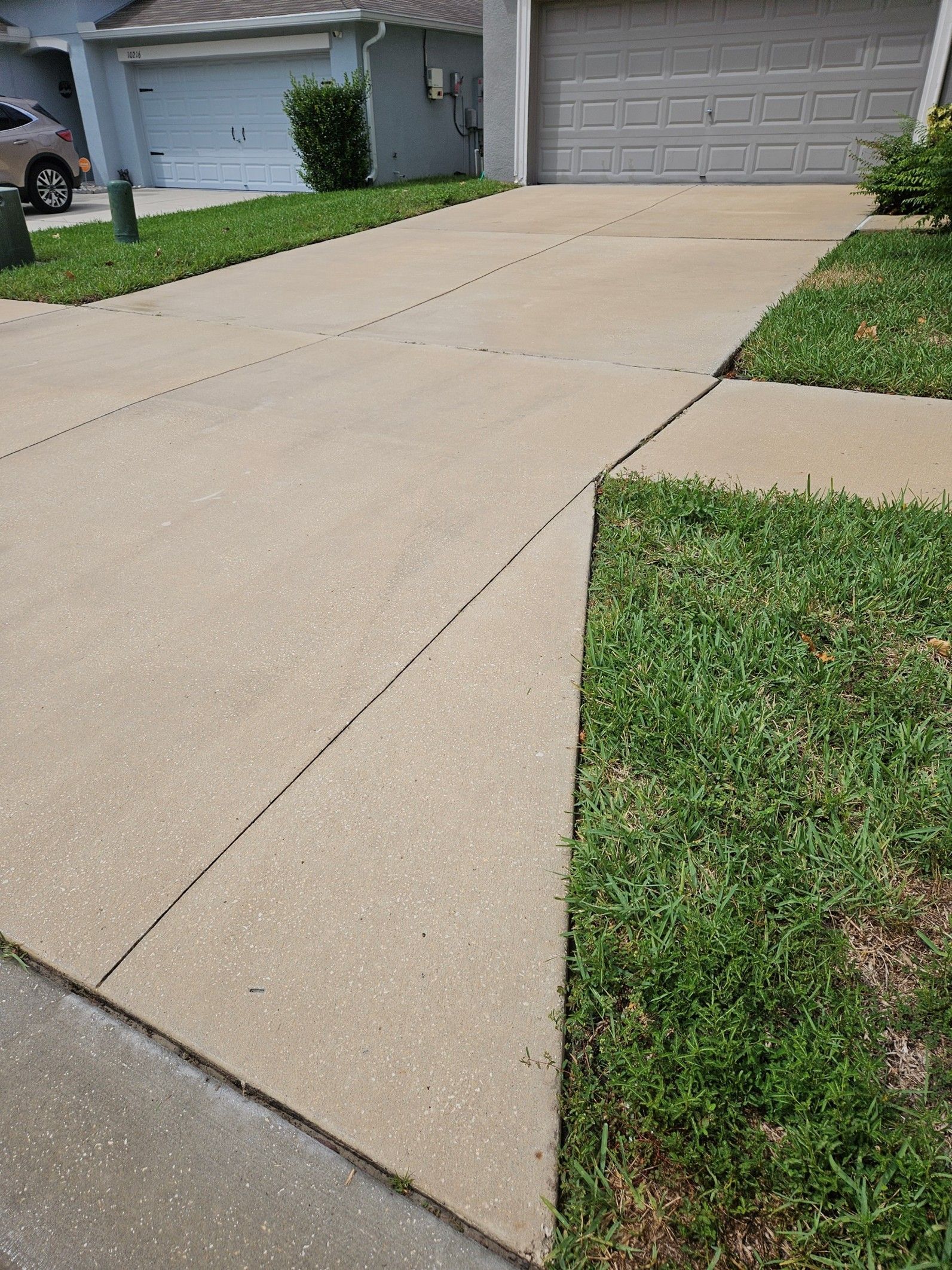 A concrete driveway leading to a closed garage door, flanked by green grass on a bright, sunny day.
