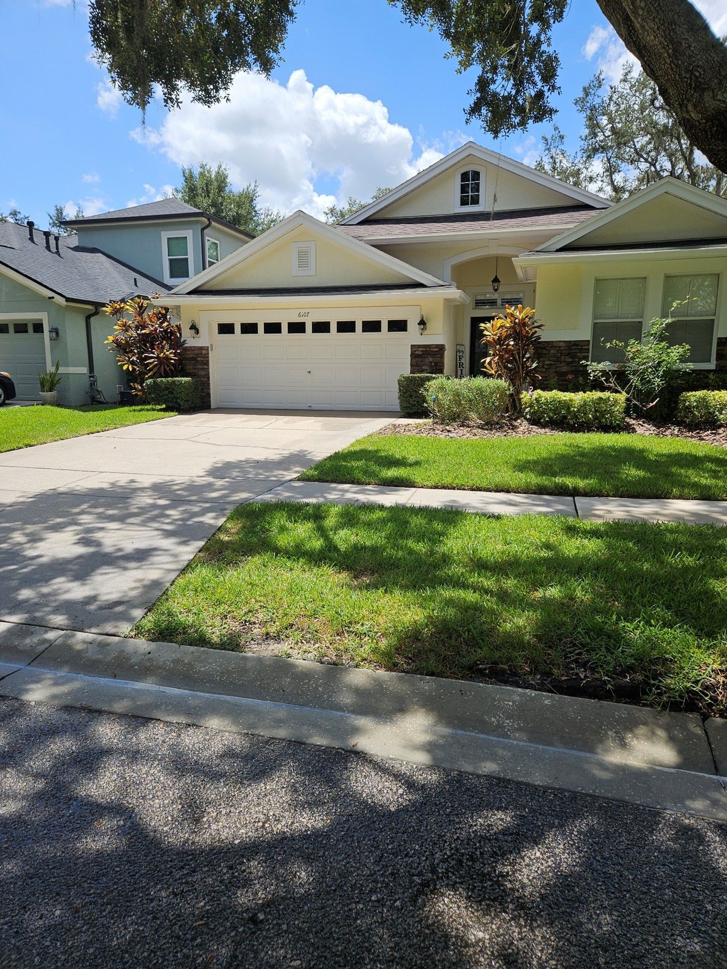 A single-story suburban house with a white garage, cream siding, stone accents, and a front lawn under a blue sky.