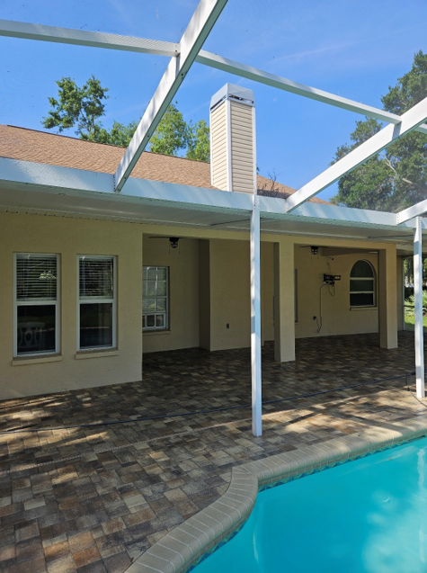 Man pressure washing a dark roof of a white house with an extension wand.