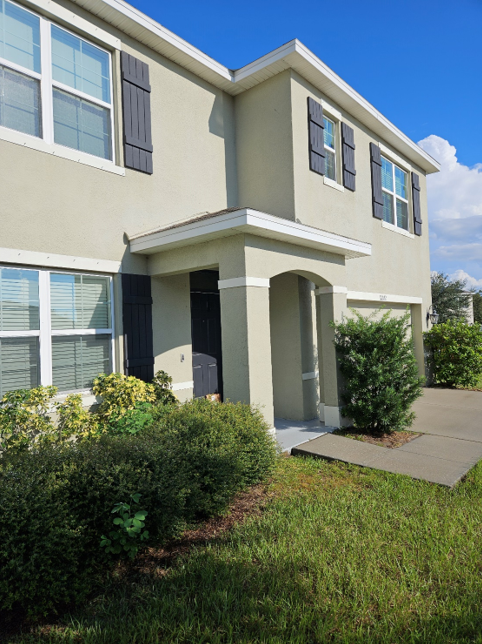 Man pressure washing a dark roof of a white house with an extension wand.