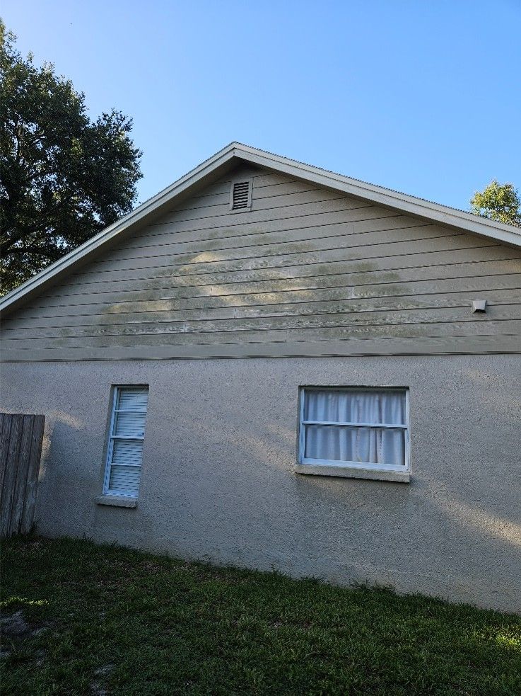 Exterior of a gray house with a gable roof, small windows, and a grassy yard under a blue sky