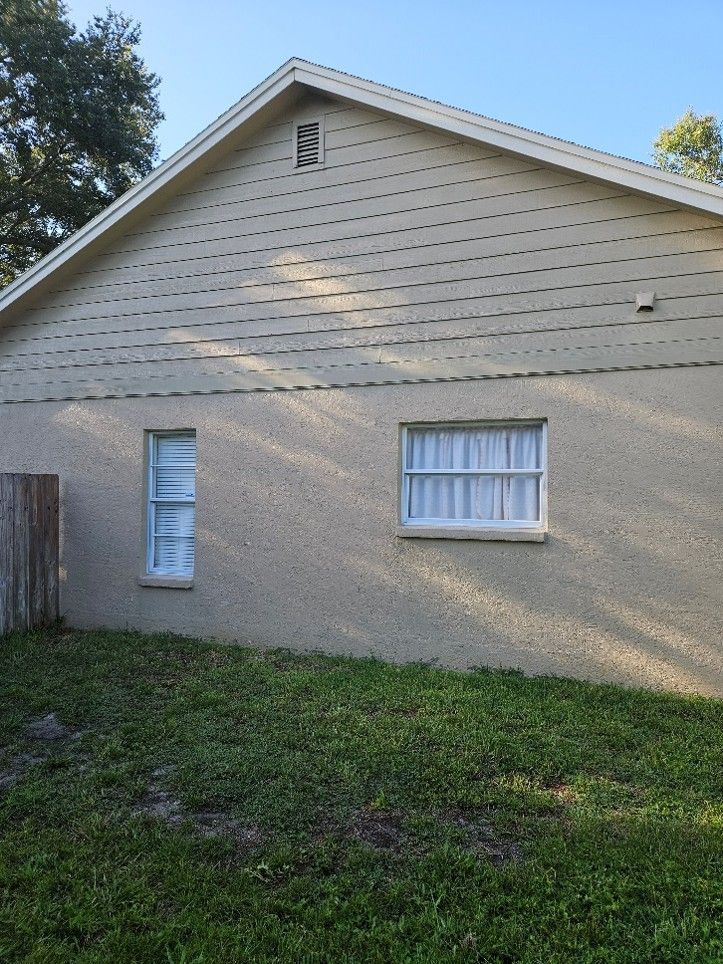 Tan siding on a house with two windows and a grassy yard under a clear sky