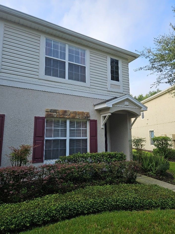 Two-story suburban house with white siding, maroon shutters, and a small front porch beside trimmed hedges