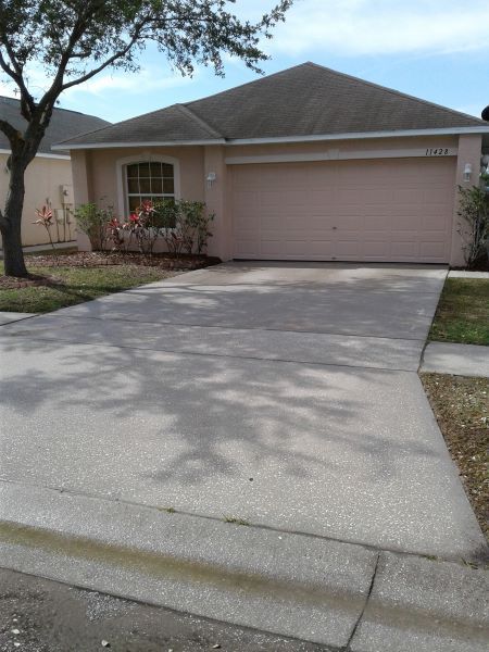 Suburban house with a two-car garage and concrete driveway shaded by a tree