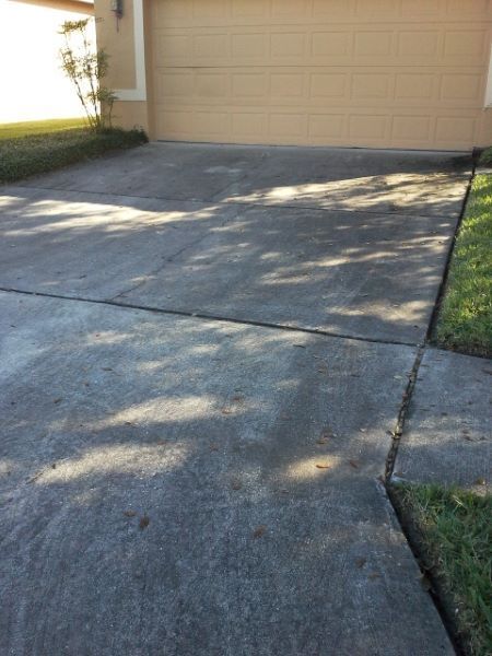 A view of a concrete driveway leading to a closed garage door with shadows from trees cast across the surface.