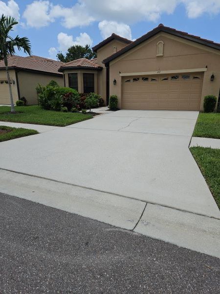 A gray, stained concrete driveway leading to a closed garage door with a lawn and tree nearby.
