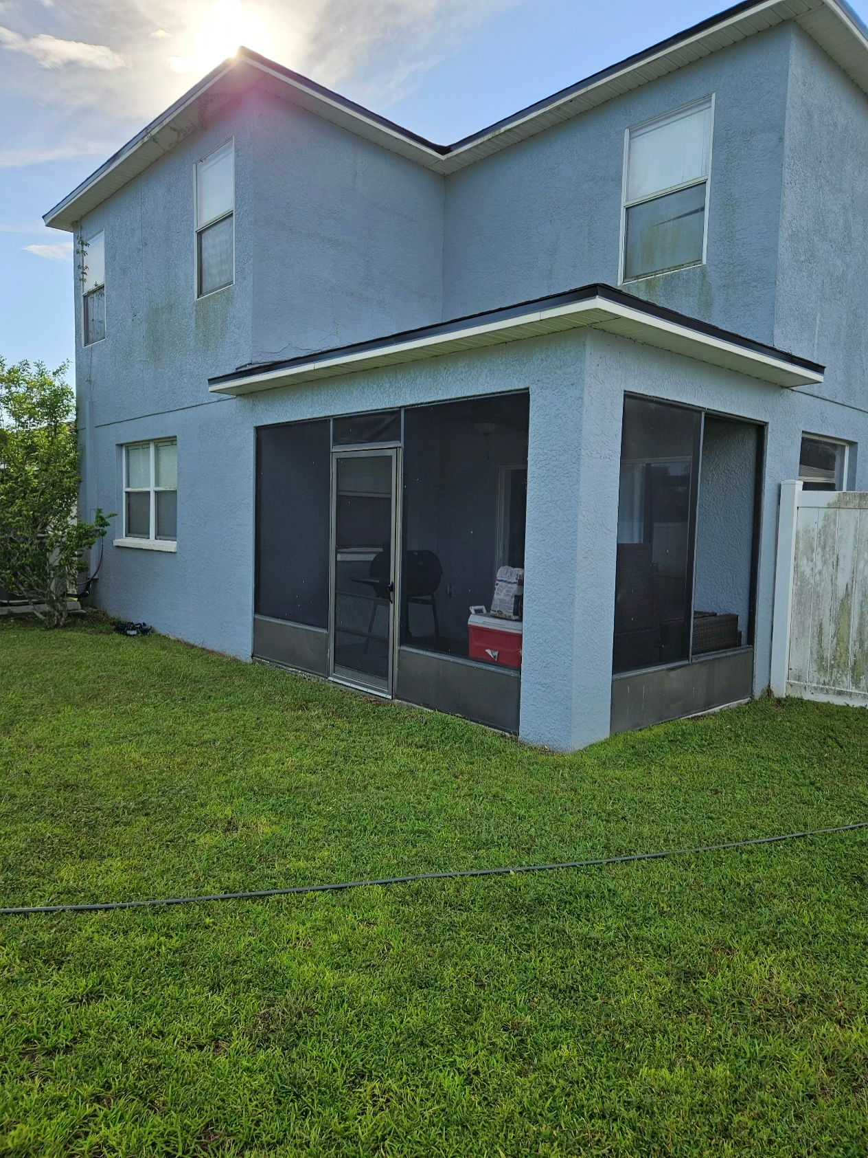 A two-story light blue stucco house with a screened-in back porch, set against a green lawn under a sunny sky.