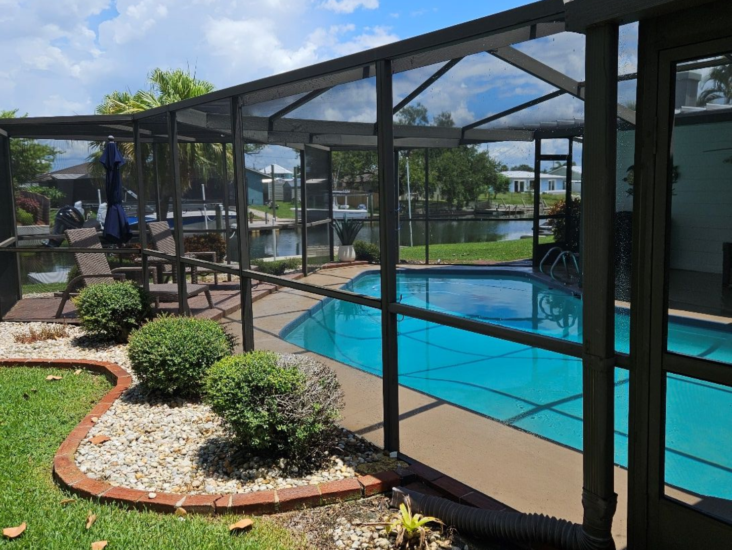 Screened-in pool area with a turquoise pool, patio, and green grass. Blue sky with clouds.