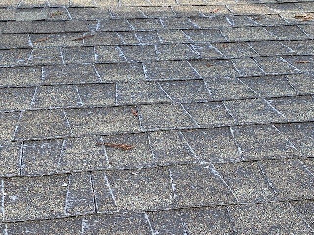Close-up of weathered asphalt roof shingles, gray and brown with white streaks.