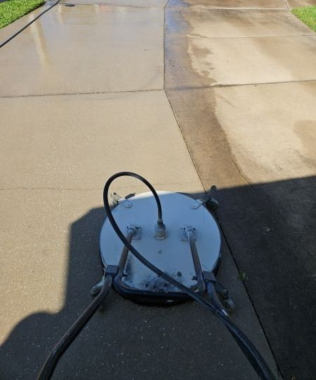 Pressure washer cleaning a concrete driveway, leaving a clean path.