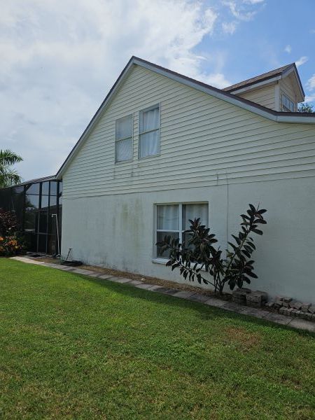 The side of a two-story home with pale yellow vinyl siding on top and a white stucco wall below, next to a lawn.
